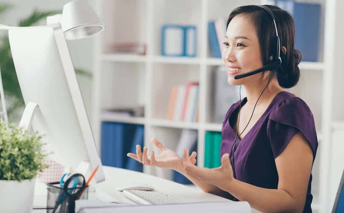  A customer service agent is sitting at her desk, wearing a headset and speaking with a customer while maintaining composure and professionalism.